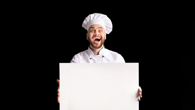 Restaurant Menu. Excited Chef Man Holding Empty White Board For Text Advertising Something Standing Over Black Background In Studio. Mockup photo