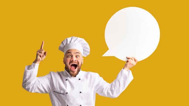 Recipe Idea. Excited Chef Man Holding Blank White Speech Bubble Pointing Finger Standing On Black Studio Background. Panorama, Mockup photo