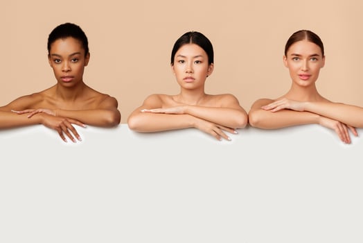 Three Multiethnic Ladies Standing Naked Posing Behind White Board For Text On Gray Background In Studio. Empty Space photo