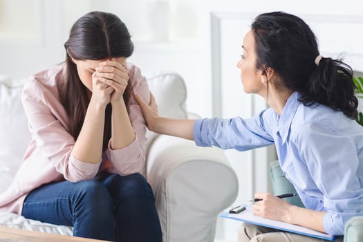 Crying woman is seated on a couch, engaged in conversation with a therapist. Both individuals seem attentive and focused on the discussion taking place. photo