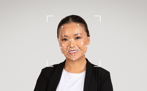 A smiling Asian woman in a black blazer poses with a facial recognition graphic displayed on her face. photo
