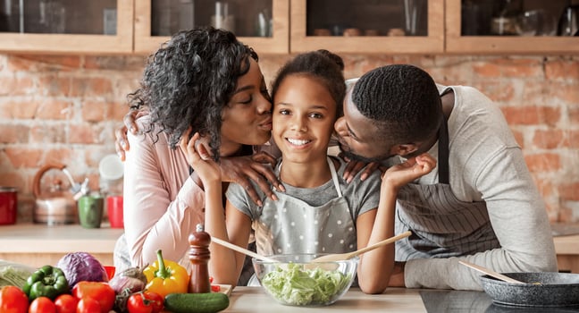 Adorable black family cooking healthy dinner together at kitchen, parents kissing daughter, panorama with copy space photo