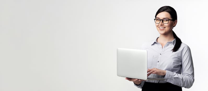 A smiling businesswoman in a white shirt holds a laptop in front of a white background. photo
