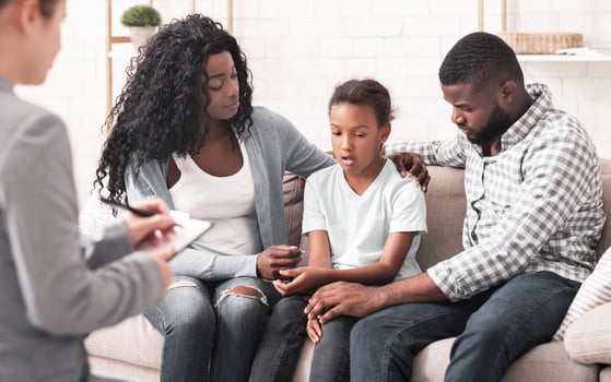 Bipolar Disorder In Children Concept. Little african american girl and her parents at reception of psychologist, kid sharing her feelings with doctor photo