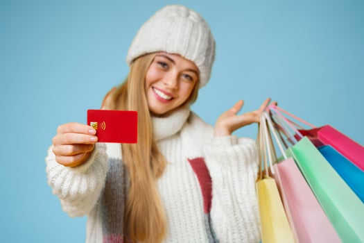 Happy young woman in white hat recommending credit card, posing with colorful shopping bags and smiling at camera, yellow background photo