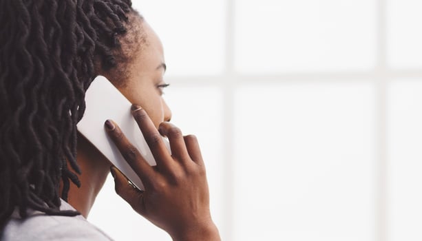 Cheerful young African American lady manager in formal wear, by the office window, speaking on the phone, copy space photo