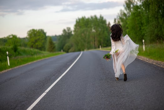 Rear view of young woman in awhite dress running on an asphalt country road photo