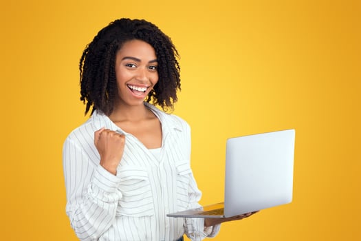 Well Done. Excited african american woman celebrating online win, great deal or business success using laptop photo