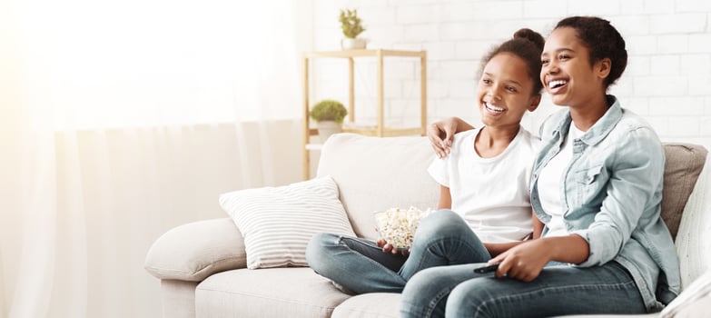 Two cheerful black girls enjoying movie, eating popcorn at home, empty space photo