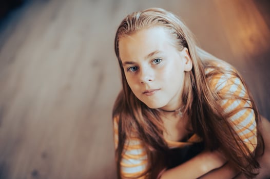 A teenage girl with long hair sits on the floor and looks up photo