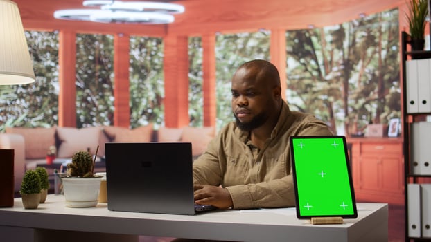 Business owner manages financial plans next to a mockup display on tablet, using annual sales analytics and reports to increase the profit. Entrepreneur does budget analysis at home. Camera B. photo