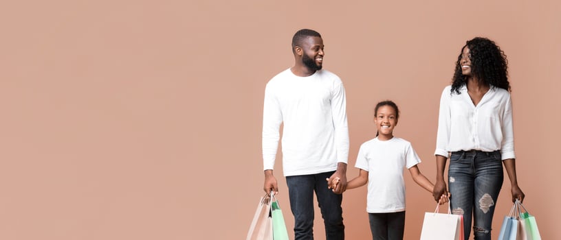 Family Shopping Concept. Happy African American parents and their daughter walking with shopper bags and holding hands in studio, yellow background. photo