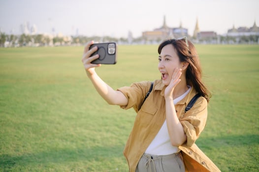 Traveler asian woman in her 30s making a livestream or selfie on smartphone while explores the grandeur of Wat Pra Kaew. Discover the religious significance and historical heritage with her. photo