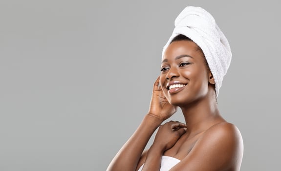 After Spa. Beautiful african woman with bath towel on head and perfect glowing skin looking aside relaxed after beauty treatment, grey background photo