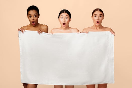 Three Shocked Diverse Models Girls Posing Holding Bath Towel Looking At Camera On White Studio Background. Body Care And Beauty. photo