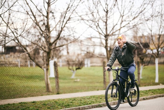 Man Waving While Riding Bike Down Street photo