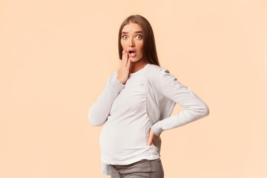 Surprised Pregnant Lady Touching Chin Looking At Camera Standing On White Studio Background. Copy Space photo