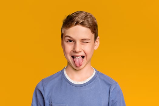 Playful teen boy winking and sticking out tongue, orange studio background photo