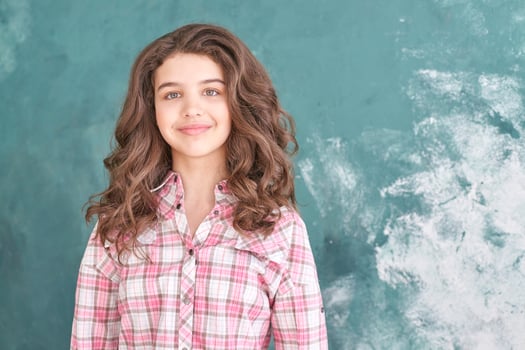 Smiling teen girl in plaid shirt posing against textured green wall. photo