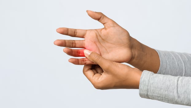 Young black woman suffering from pain in hand and massaging her painful finger, grey background photo