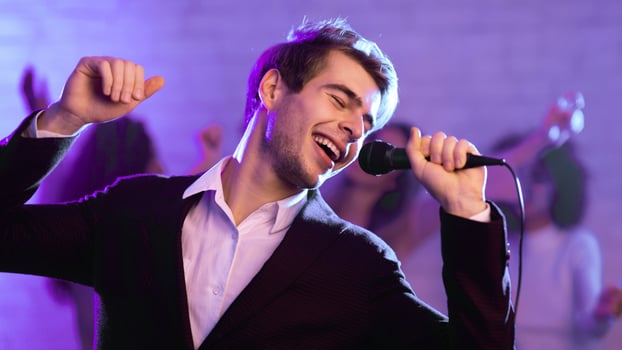 Karaoke Party. Young Man Singing Song Holding Microphone Having Fun Partying At Night Club With Friends. Panorama, Blue Light photo
