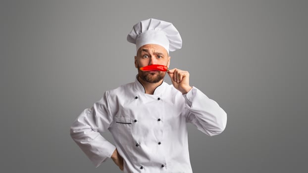 Funny Chef Guy Holding Red Chilli Pepper Near Face Like Moustaches Posing Having Fun Over Black Studio Background. Panorama photo