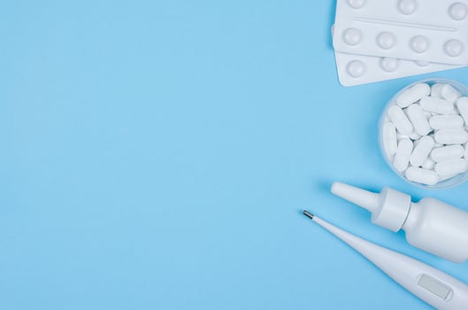 Blisters with tablets, a thermometer, and nasal spray on blue background. Flat lay with copy space. Stock photo
