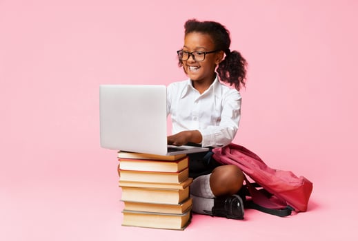 Cheerful African American Schoolgirl Sitting At Laptop Doing Homework Over Yellow Background In Studio. photo