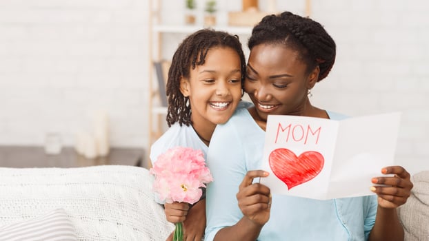 I Love You Mom. African girl congratulating her mom with pink flowers and card, free space photo