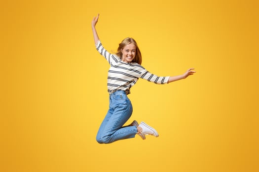 Happy teenage girl jumping in the air, pretending she is flying. Orange studio background with free space photo