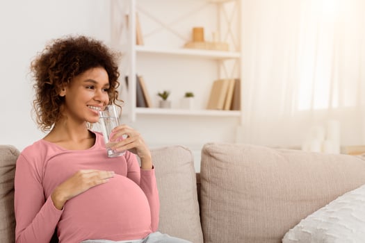 Water balance. Pregnant woman drinking water, resting on sofa at home, empty space photo