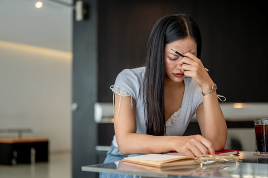 A stressed Asian woman feeling headache and eye strain while reading a book in a coffee shop. photo