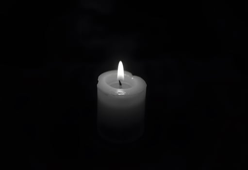 A single candle is lit in the dark photo