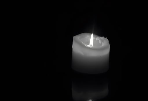 A single white candle is lit on a black surface photo