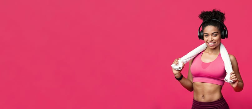 Gym, fitness concept. Smiling sporty black girl with towel and earphones over red background, panorama with copy space photo