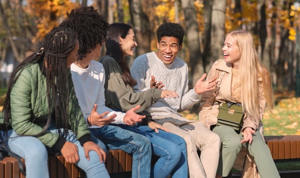 Black cheerful guy telling his multiracial friends funny story, spending time together in public park photo
