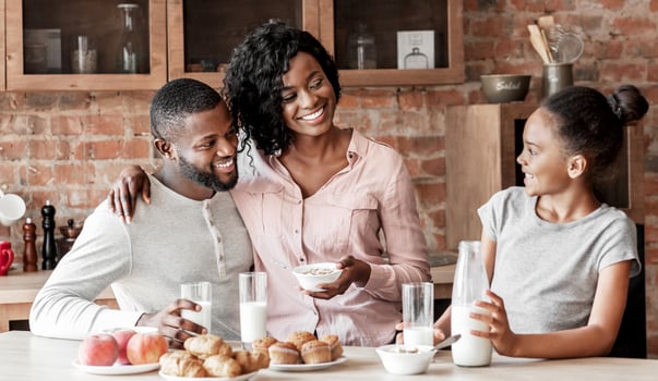 Adorable african family of three having breakfast at kitchen, eating and talking, copy space photo