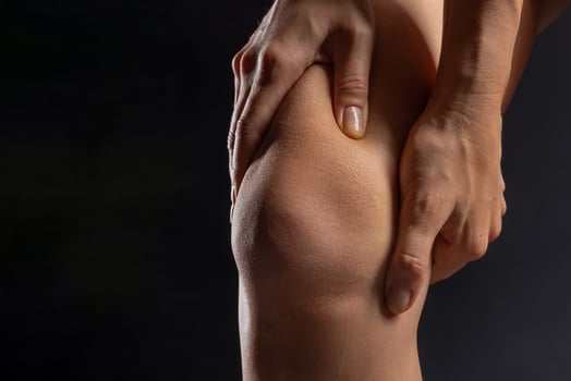 woman hands close up pressing on knee joint on dark background, knee pain concept photo