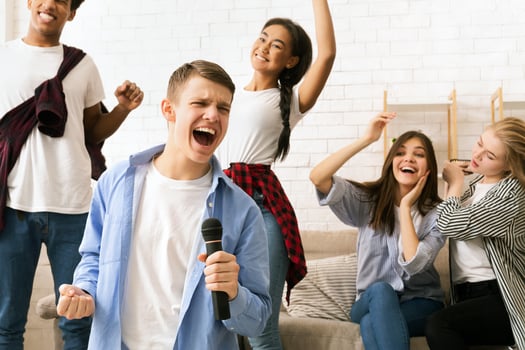 A diverse group of friends standing together on a stage, singing into a microphone, dressed in casual clothing and are passionately performing for an audience photo