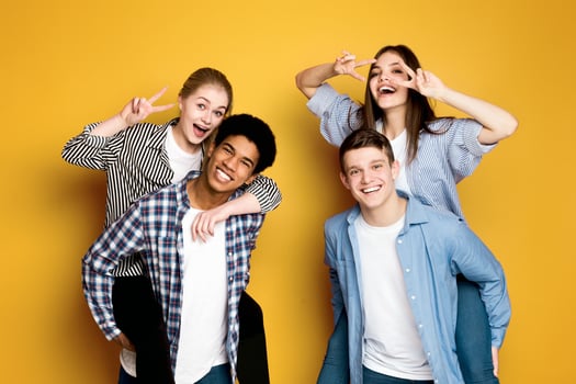 Four cheerful multiethnic teenagers, two guys, and two girls, huddle together against a bright yellow backdrop. photo