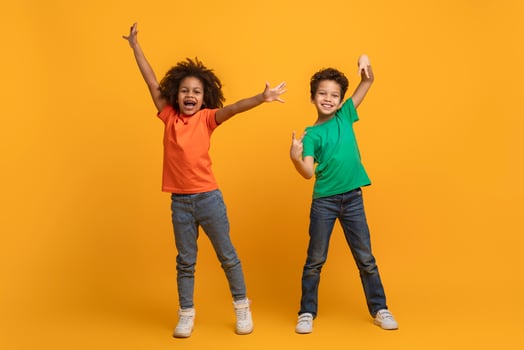 Two young African American siblings are standing with their arms raised in excitement and big smiles on their faces, expressing joy and celebration against a vibrant yellow backdrop. photo