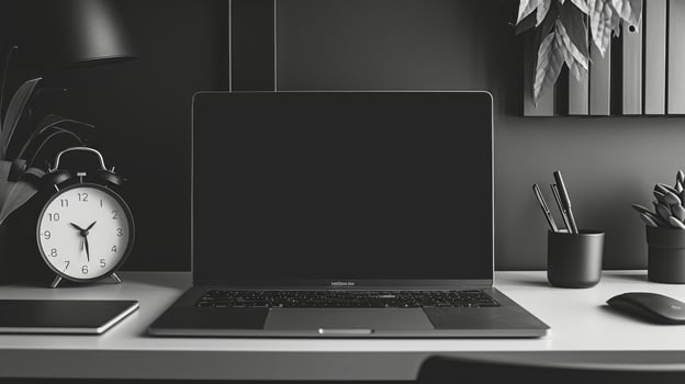 A monochromatic desk display featuring a sleek silver laptop matte black accessories and a simple white clock demonstrating the beauty of a minimalistic aesthetic photo