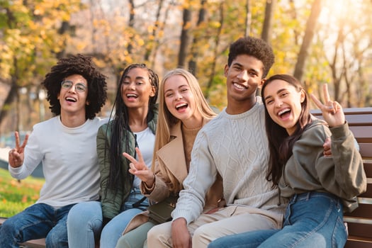 Positive international teenagers enjoying weekend at public park, sitting on bench and posing at camera photo