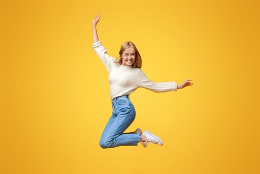 Enjoying youth. Cute teenage girl having fun jumping in air on orange background photo