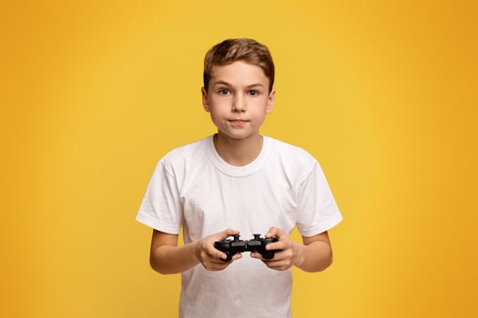 Concentrated boy playing game with joystick on orange studio background photo