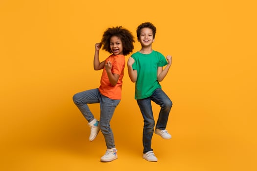 Two African American children, both young and full of energy, are captured mid-air as they jump together. Their bodies are lifted off the ground, displaying pure joy and excitement in their faces. photo