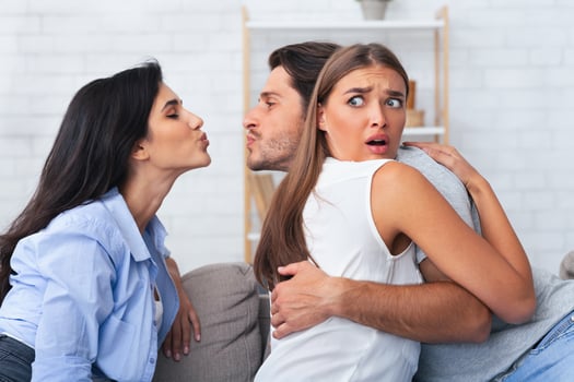 Love Triangle And Jealousy. Cheating Boyfriend Kissing A Girl While Hugging His Girlfriend Sitting Together On Couch Indoor. photo