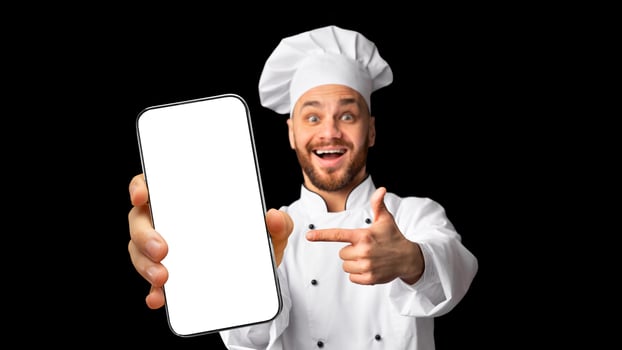 Excited Cook Man Showing Phone Empty Screen Recommending Restaurant Food Delivery App Service Standing On Black Studio Background. Panorama, Mockup photo
