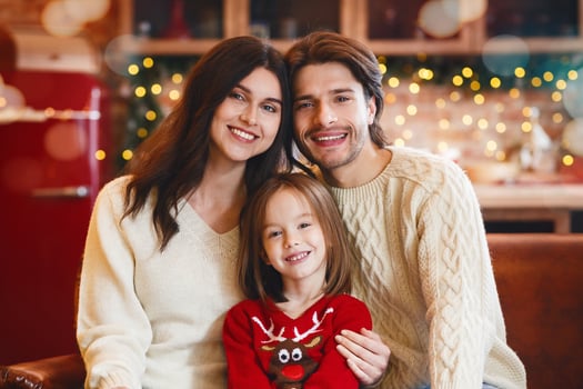 Affectionate little family getting ready for New Year celebration, sitting on sofa, smiling at camera over decorated kitchen, free space photo