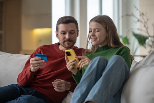 Online home shopping. Interested couple pays for purchases with bank card using phone sits on couch. photo
